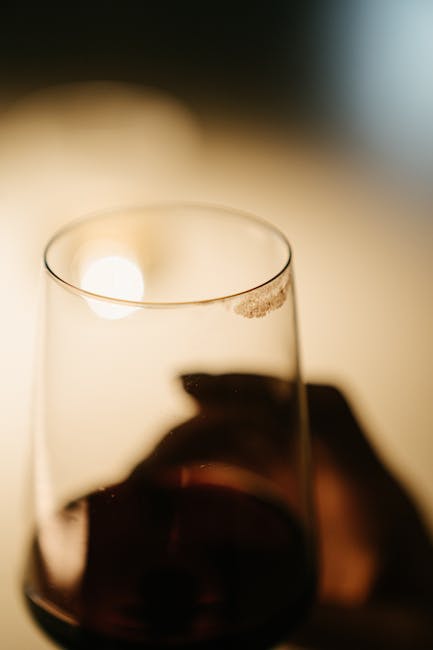 Close-up of a transparent wine glass filled with red wine placed on a smooth, polished wooden surface in a well-lit room. The glass shows a slight reflection of light, and the background is softly blurred, emphasizing the clarity of the glass and the rich, deep color of the wine. The setting suggests a domestic space, with a focus on surface cleaning and maintenance. The image underscores the importance of professional hygiene and deep cleaning services offered by iCarpet Cleaners, particularly in relation to removing stains like red wine from carpets and surfaces in residential environments.